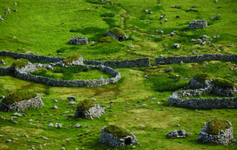 Aerial view of a green landscape with ruined stone structures and walls
