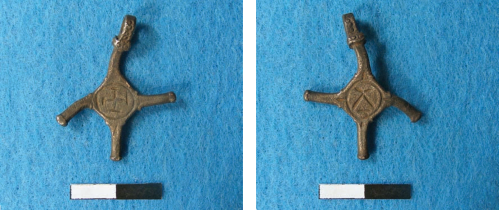 Photo of a small, cross-shaped metal pendant, with one arm bent
