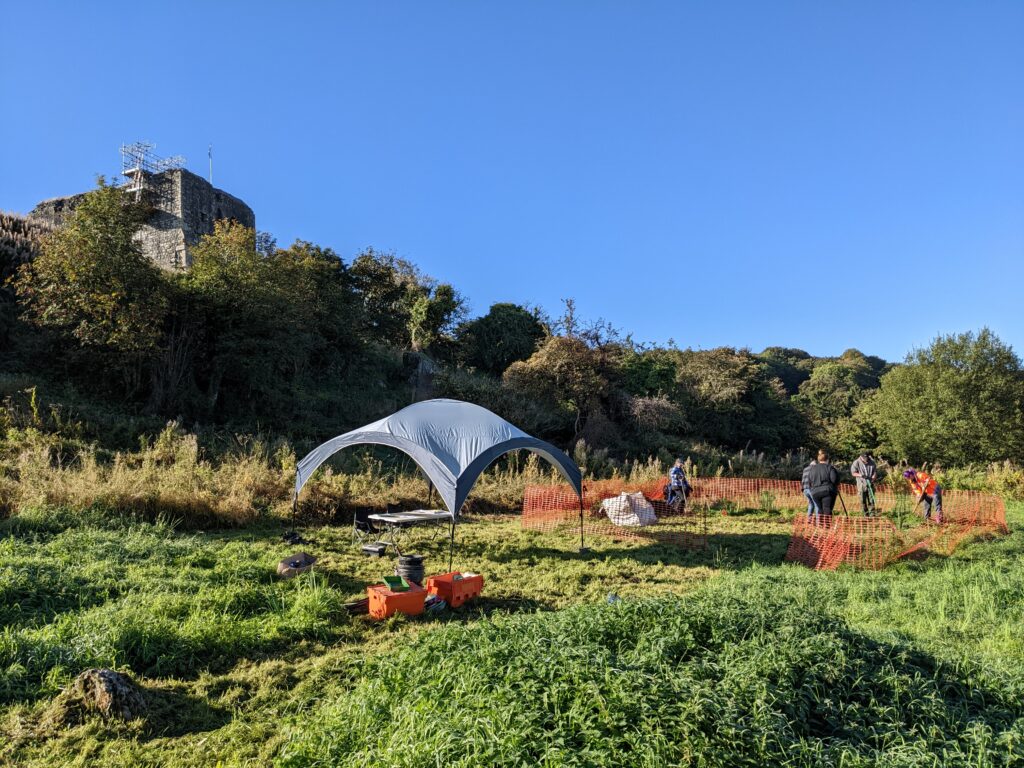 People investing a field below a ruined castle - a tent is set up