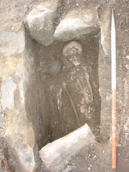 Photo of a stone-lined cist burial with a skeleton, urn and sword visible