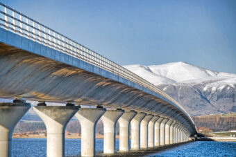 Photo of a stone road bridge crossing a river with snowy mountains in the background