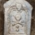 Photo of a gravestone with a skull and crossbones on it, uncovered from a trench in the ground