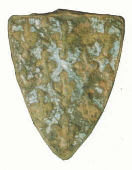 a close-up shot of a small shield-shaped metal pendant with trace of light blue heraldry