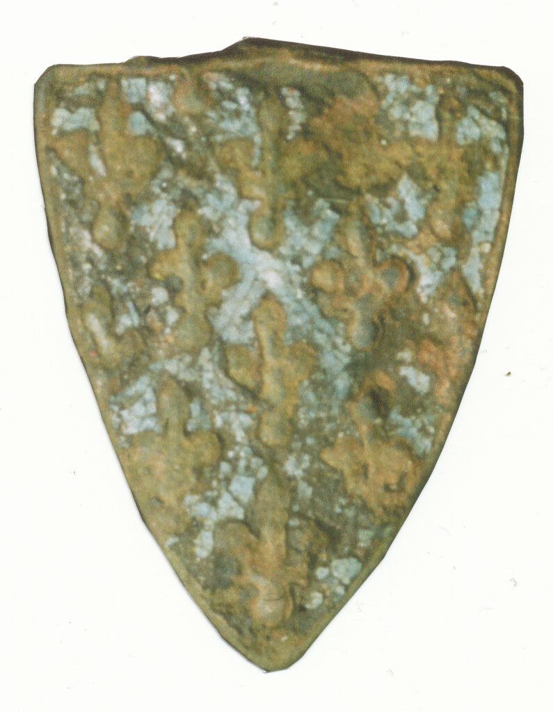 a close-up shot of a small shield-shaped metal pendant with trace of light blue heraldry 