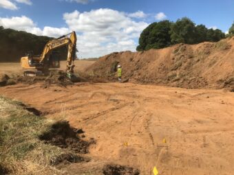 Photo of a large pit on a construction site with a big yellow digger in the background