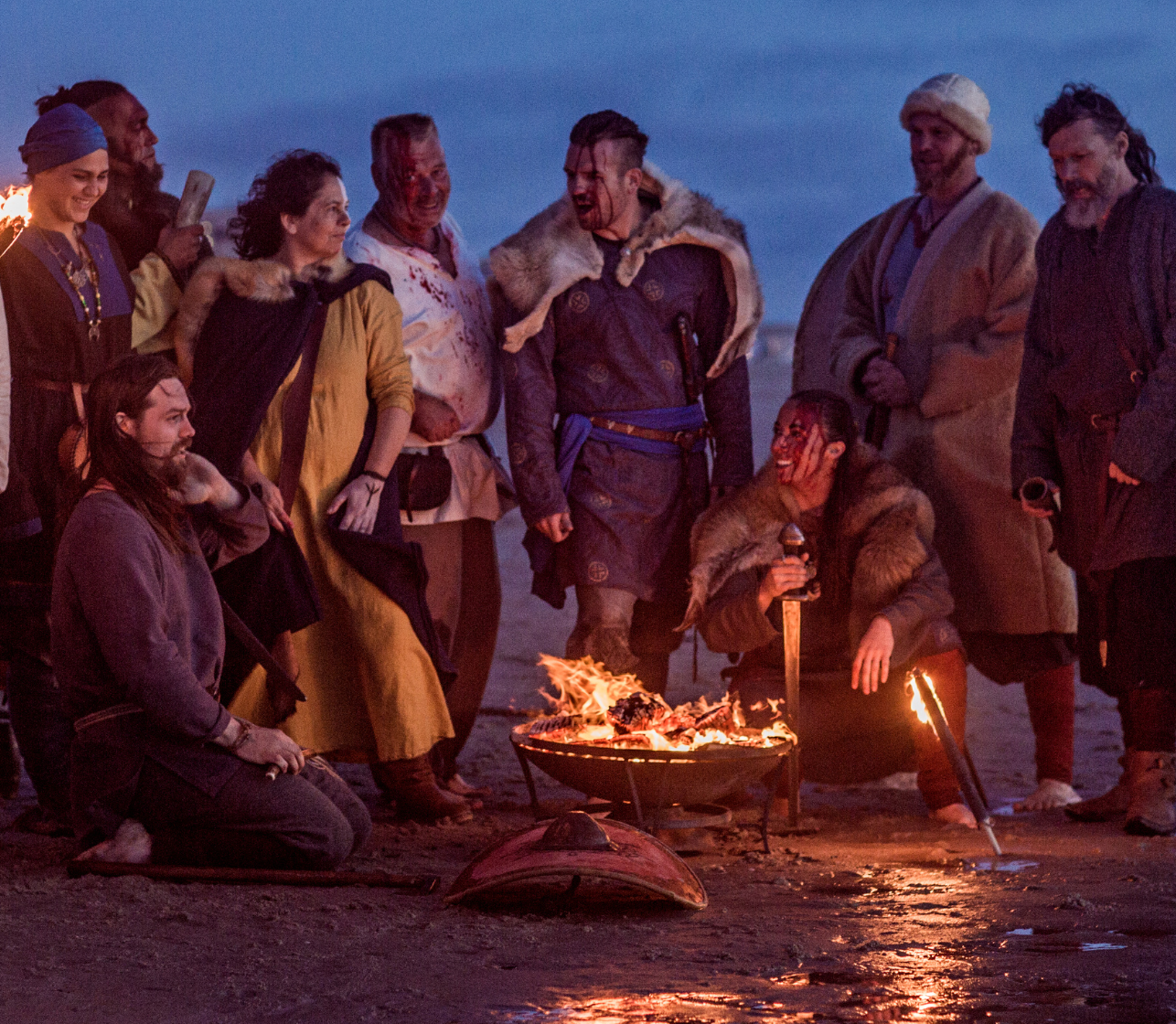 People dressed as Vikings standing around a fire on a beach