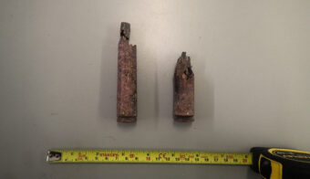 Photo of two old bullet casings on a grey table with a measuring tape underneath them