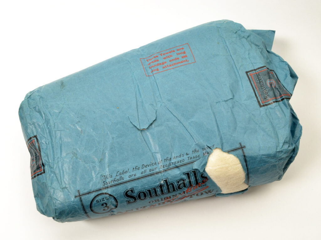 Photo of an early 20th-century sanitary towel, in a blue paper package with the words "Southall Sanitary Towel" printed in black on the front