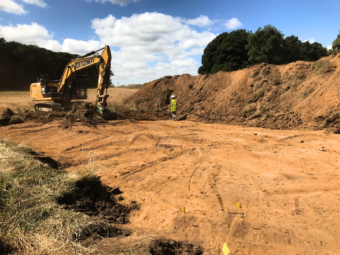 Photo of a large pit on a construction site with a big yellow digger in the background
