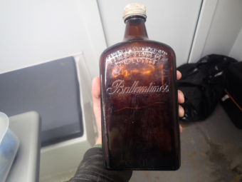 Photo of a hand holding a large square whisky bottle dug out of the ground