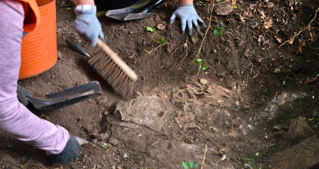 Two people leaning over a trench - one is using a shovel to brush it