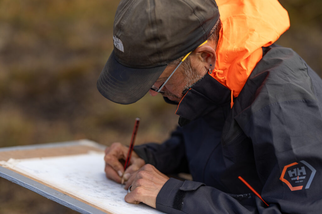 Person wearing outdoor clothing writing on a large piece of paper