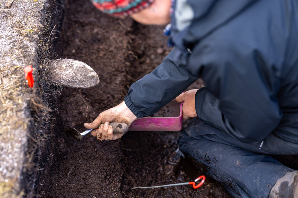 Person wearing waterproofs using a trowel in a trench