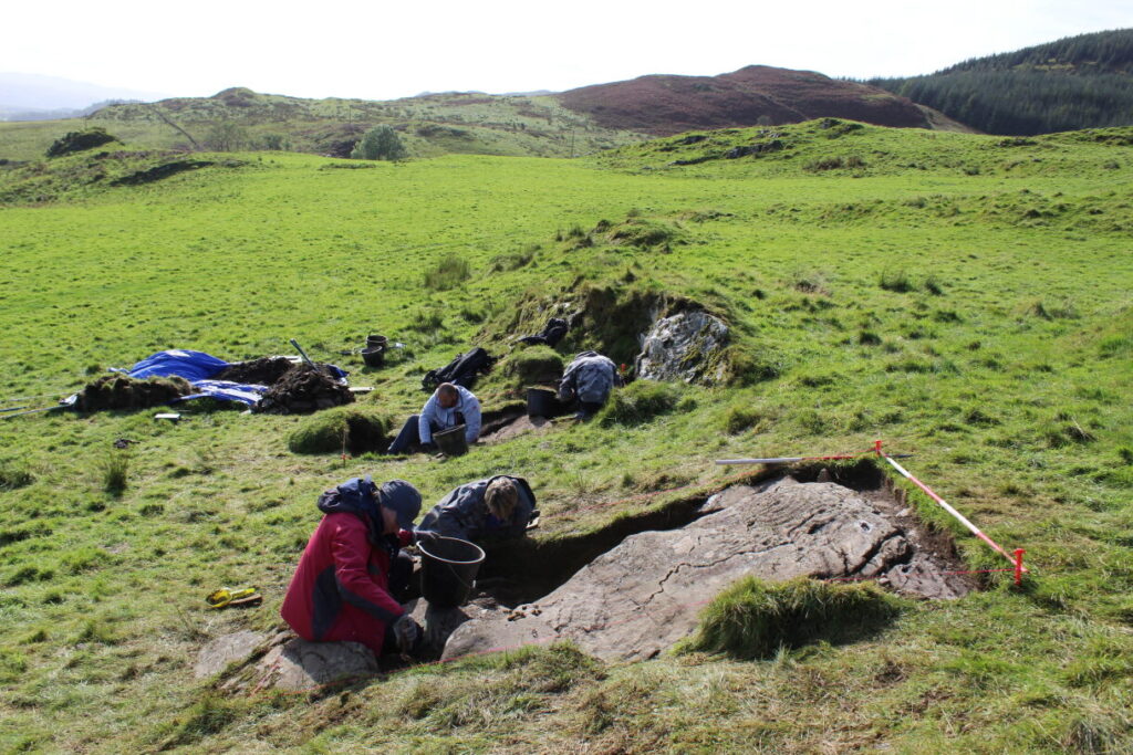 Several people digging in two trenches in a rural landscape