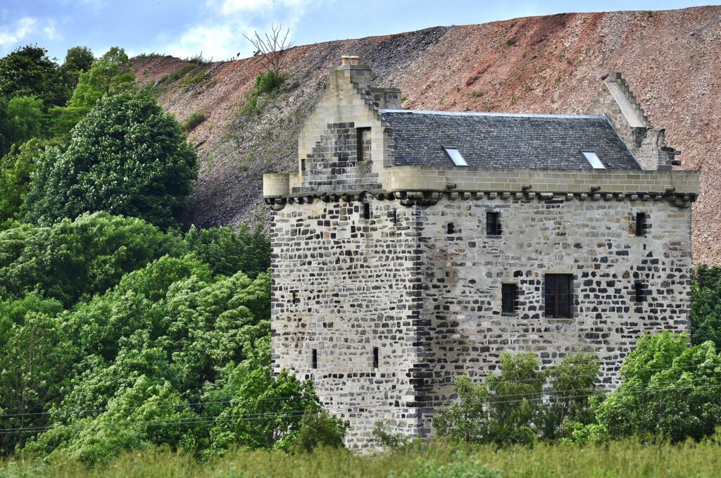 Photo of a square, stone-built tower house with a hill in the distance