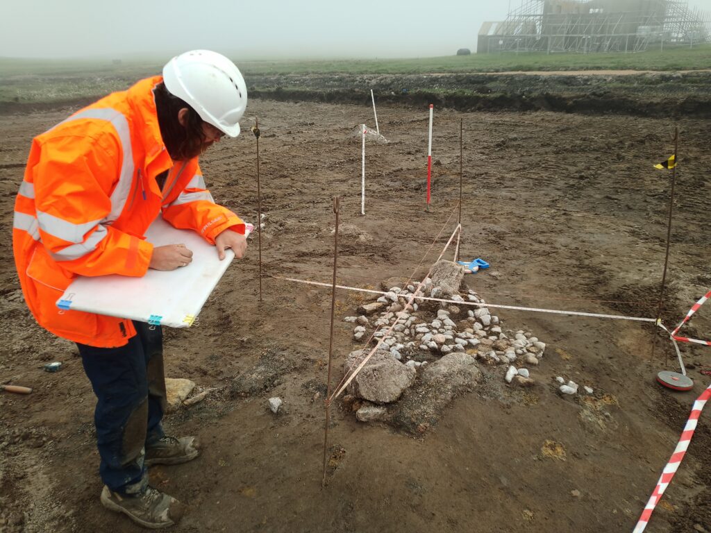 A person wearing high-visibility clothing drawing a collection of stones and quartz pebbles in the ground at the large excavation site  