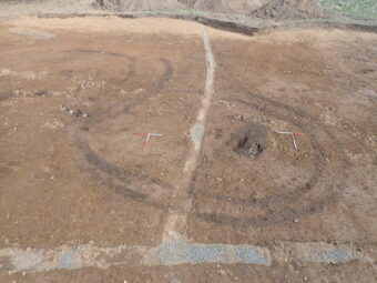 Aerial photo of an archaeological dig site, with the foundations of two prehistoric roundhouses visible in the dirt