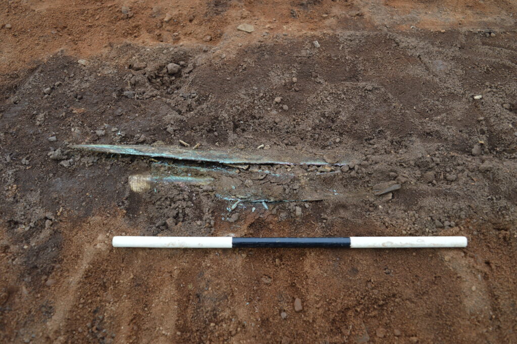 Photo of a Bronze Age sword peeking out from the dirt in an archaeological trench