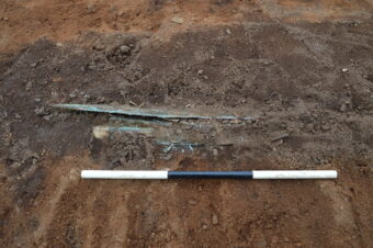 Photo of a Bronze Age sword peeking out from the dirt in an archaeological trench