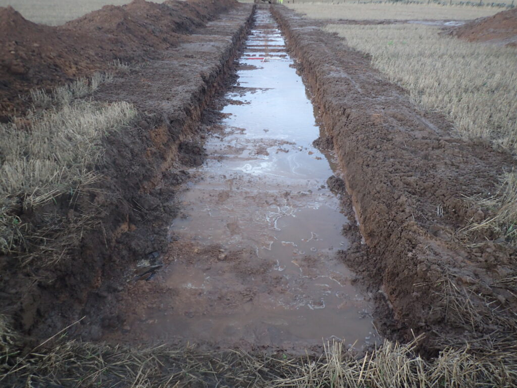 Photo of a rectangular trench in a field filled with water