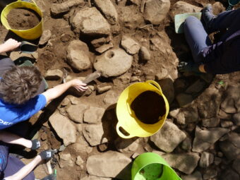 Photo of people revealing a historic paved surface in an archaeological trench