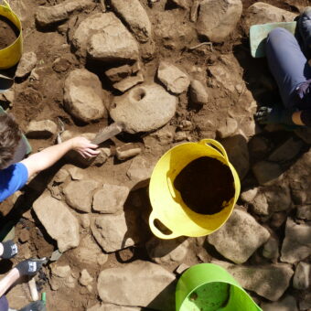 Photo of people revealing a historic paved surface in an archaeological trench