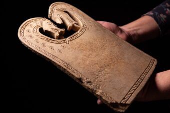 Photo of hands holding a weaving plaque with two dragon or serpent heads at the top