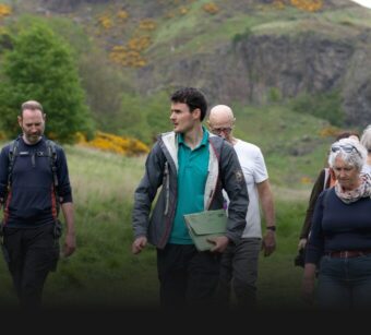 People in a grassy environment listening to a guide