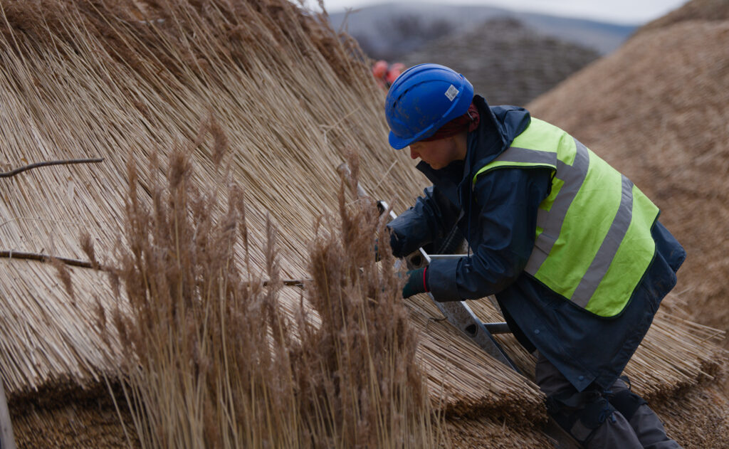 Person wearing high-vis and a helmet helping with the construction of the Iron Age-inspired village