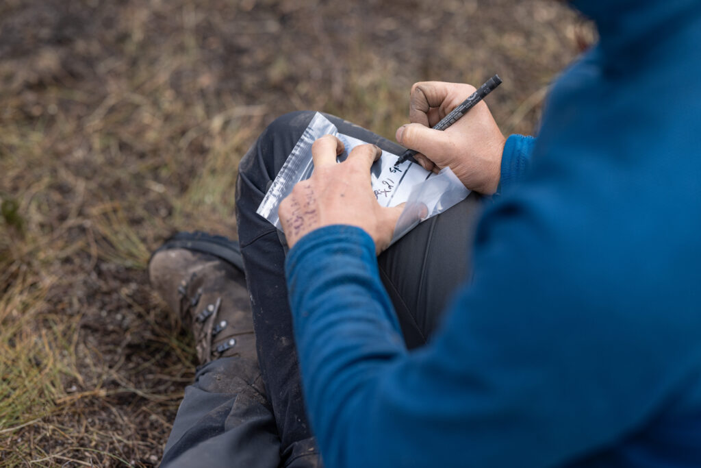 Person wearing outdoor clothing writing something on a small plastic bag