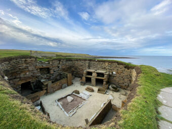 Photo of the interior of a Neolithic stone house by the sea, with an internal hearth and shelves visible