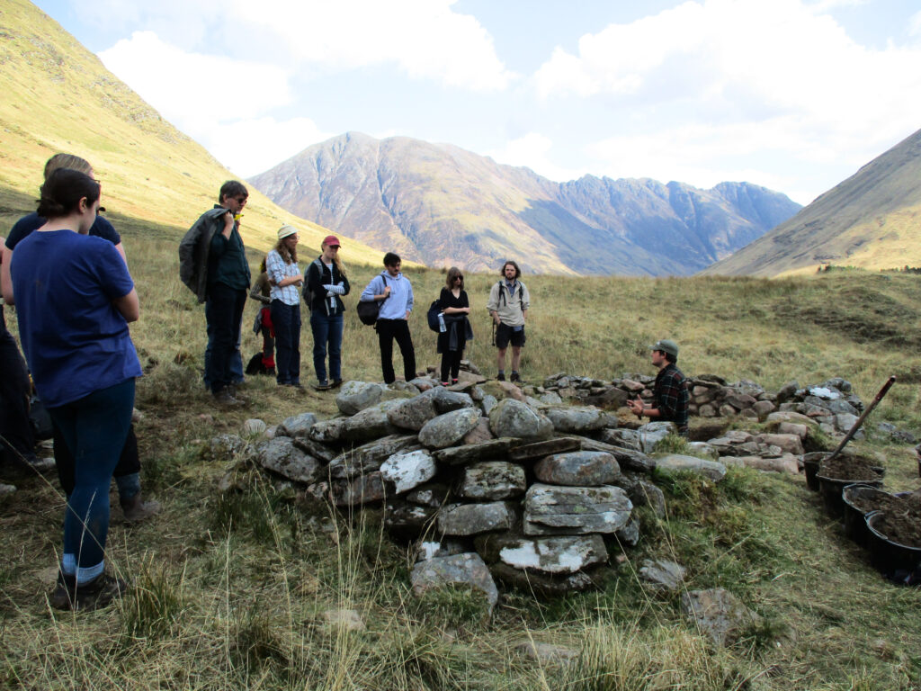 Several people in a mountain landscape standing around a ruined stone structure