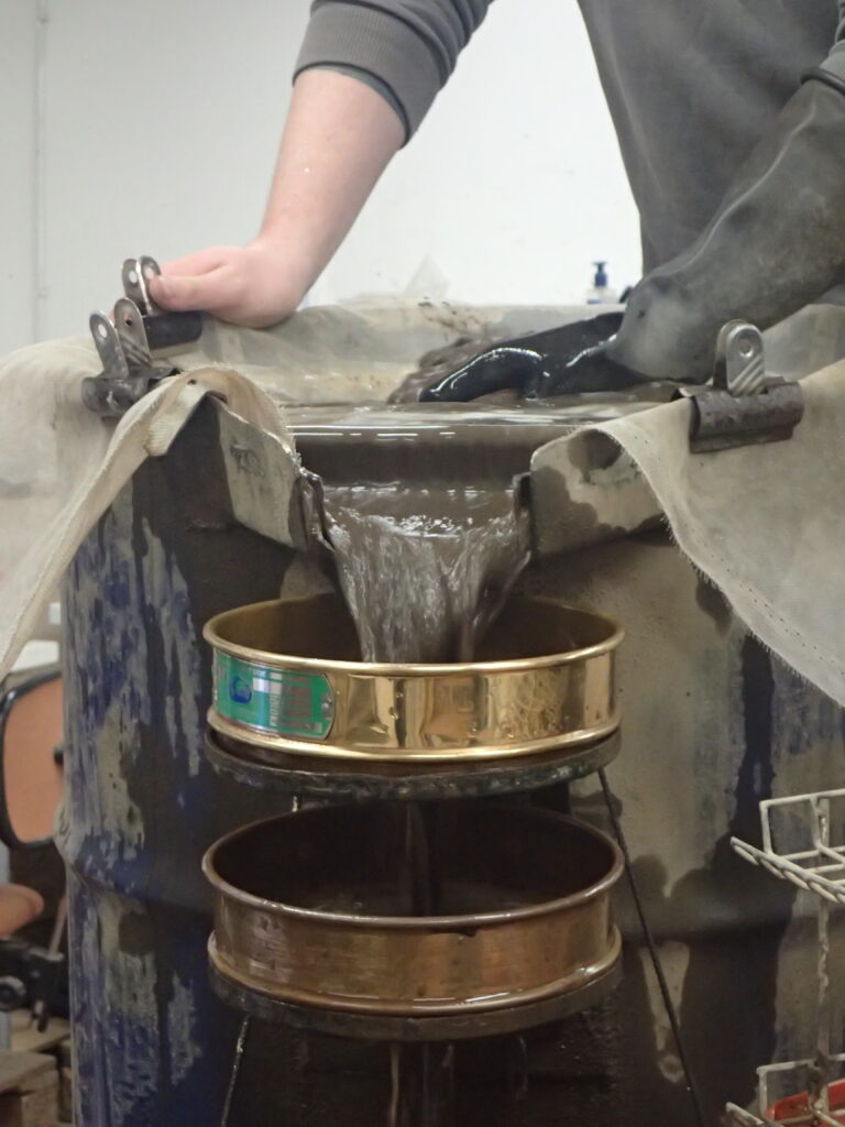 Photo of brown water being passed through a stacks of gold metal seives 