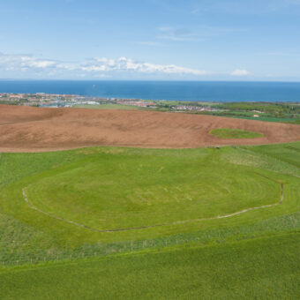 Aerial view of a site with outlines of the Neolithic structures marked out in coloured concrete in the grass