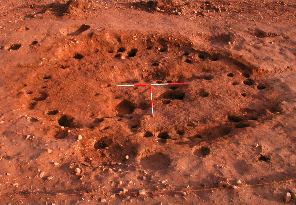 Several holes in the ground which form a circle - a measure rod laying on top