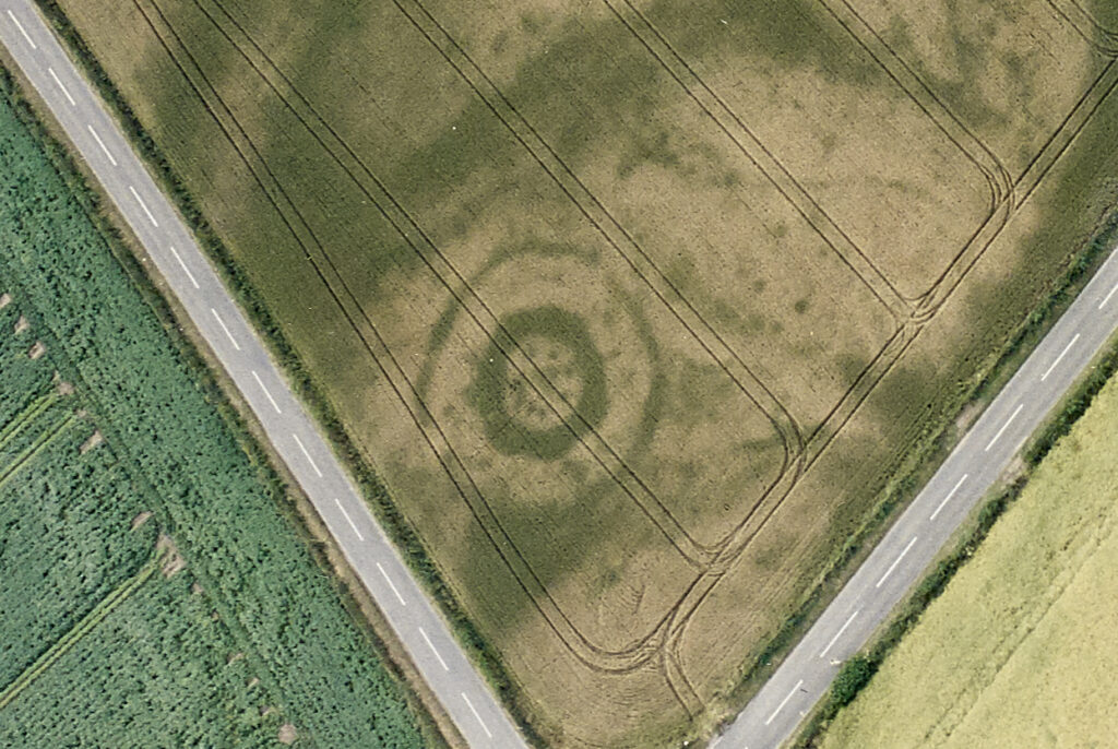 Aerial photo of a cropmark site showing a prehistoric circular enclosure in the corner of a field