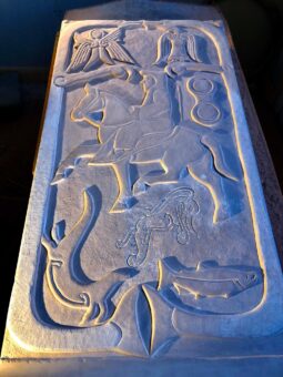 Photo of a replica carved stone depicting a man in robes on horseback, with angels, birds and beasts around him