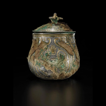 An old, decorated, round, silver-gilt, lidded vessel wrapped in scraps of textiles