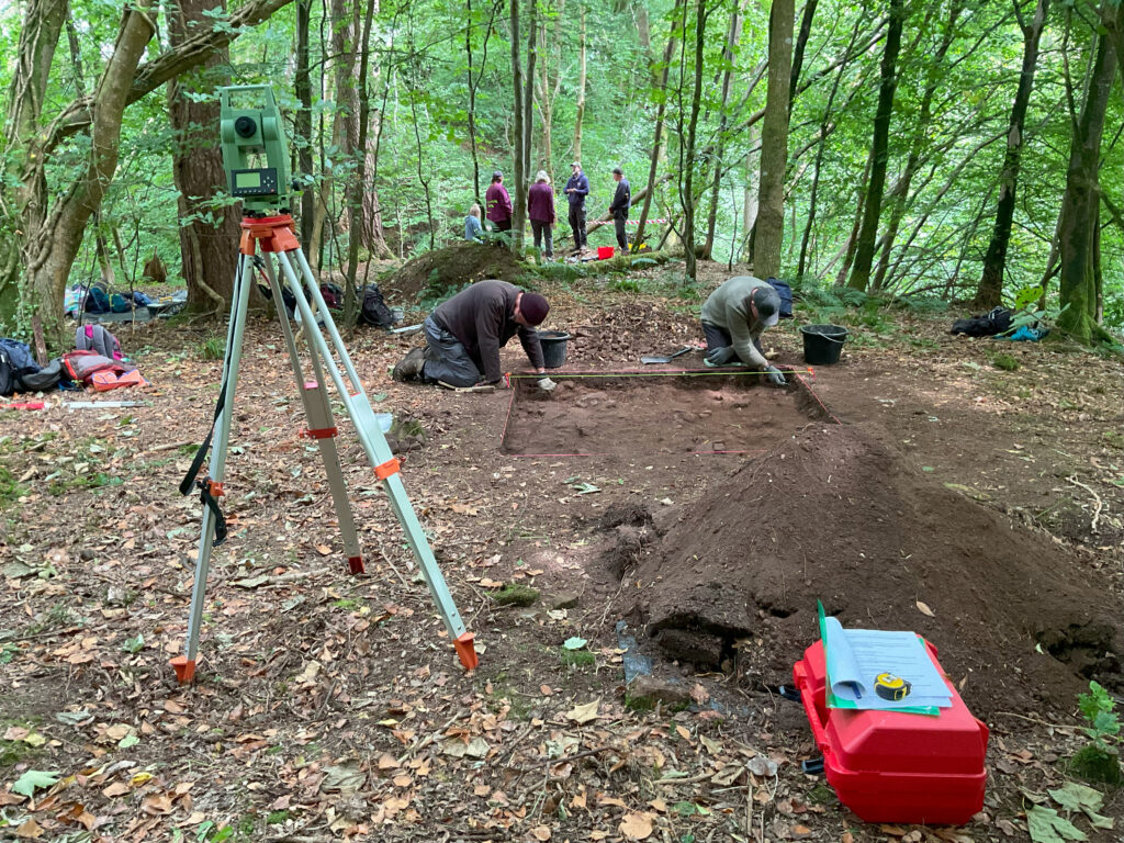 Photo of a laser scanner on a tripod and a red box with measuring equipment at an archaeological dig site 
