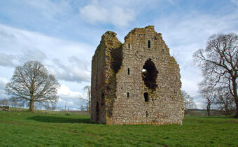 Photo of the square-built stone remains of a castle or tower in a field