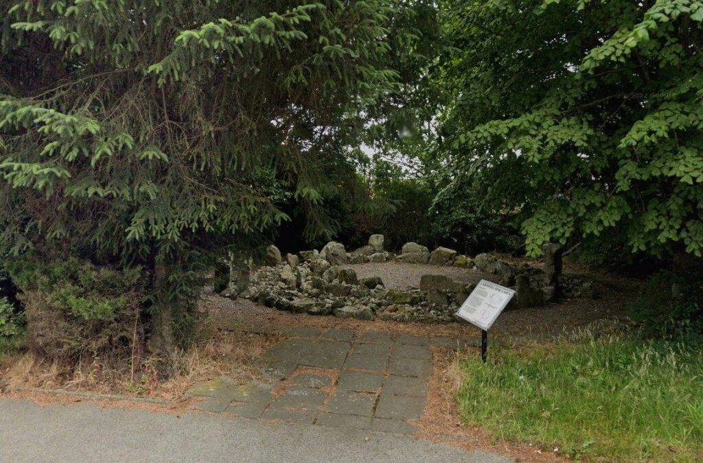 Photo of a bronze age ring cairn on a modern housing estate with an interpretation board nearby