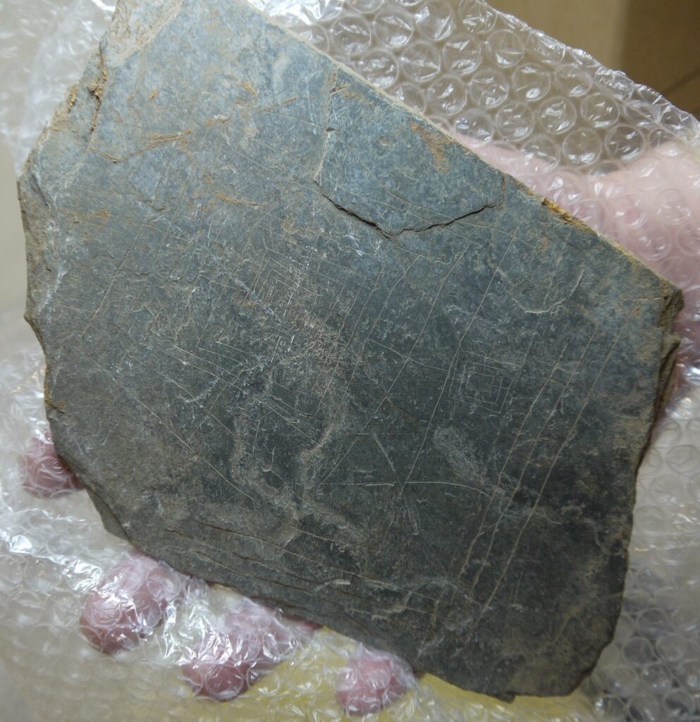 Photo of a flat piece of slate carved with thin straight lines forming a gaming board.