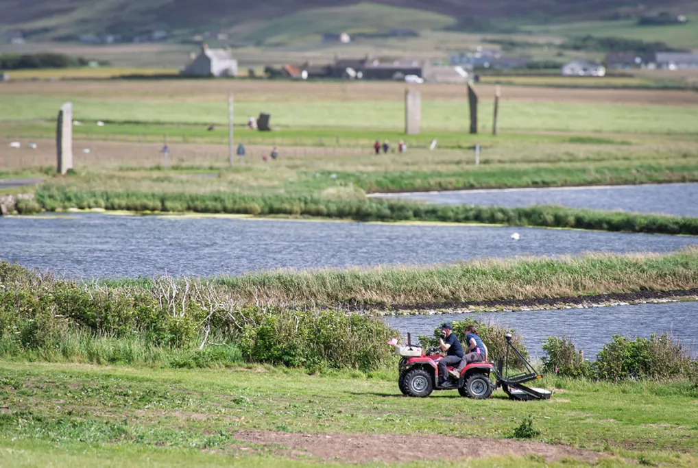 People on a tractor with large standing stones in the background