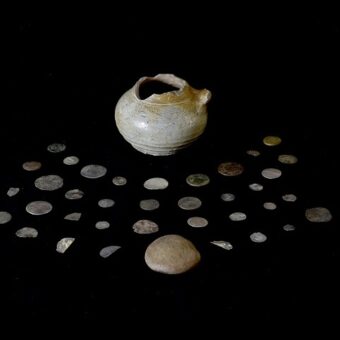 Several old coins around an old pot