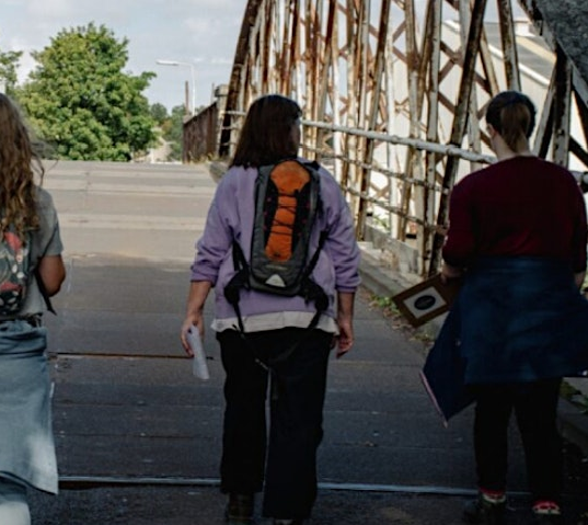 People walking over a bridge holding maps and backpacks