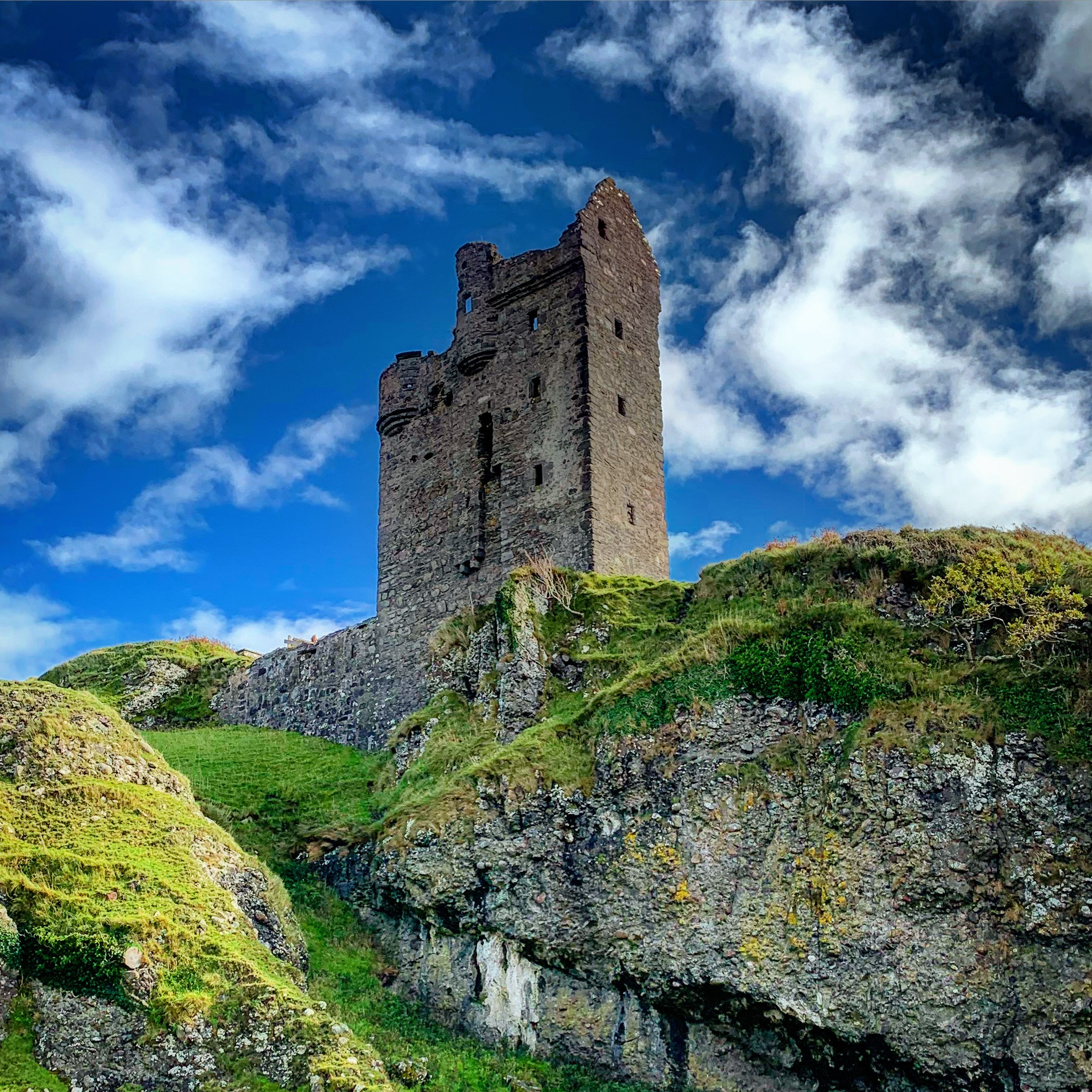 Looking up at a ruined stone tower on a cliff top