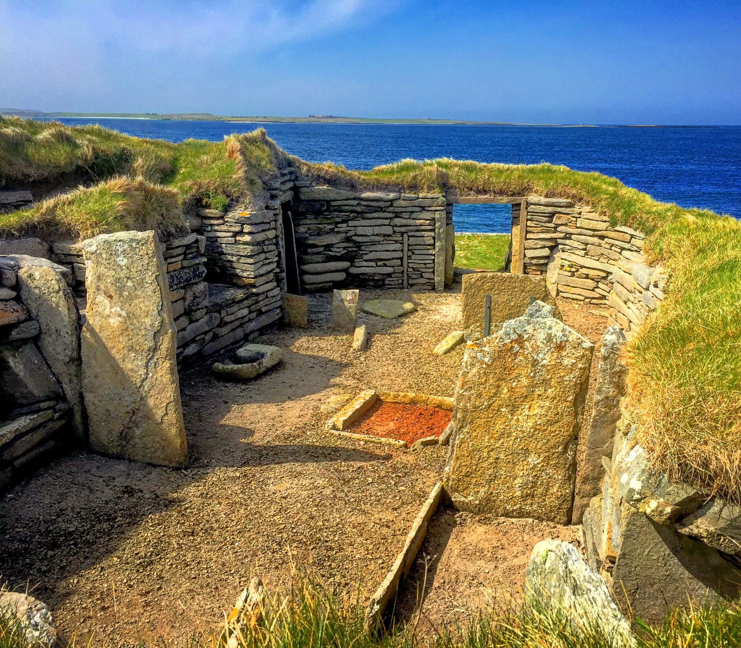 Photo of the remains of a prehistoric house by the sea, with turf-topped walls still visible
