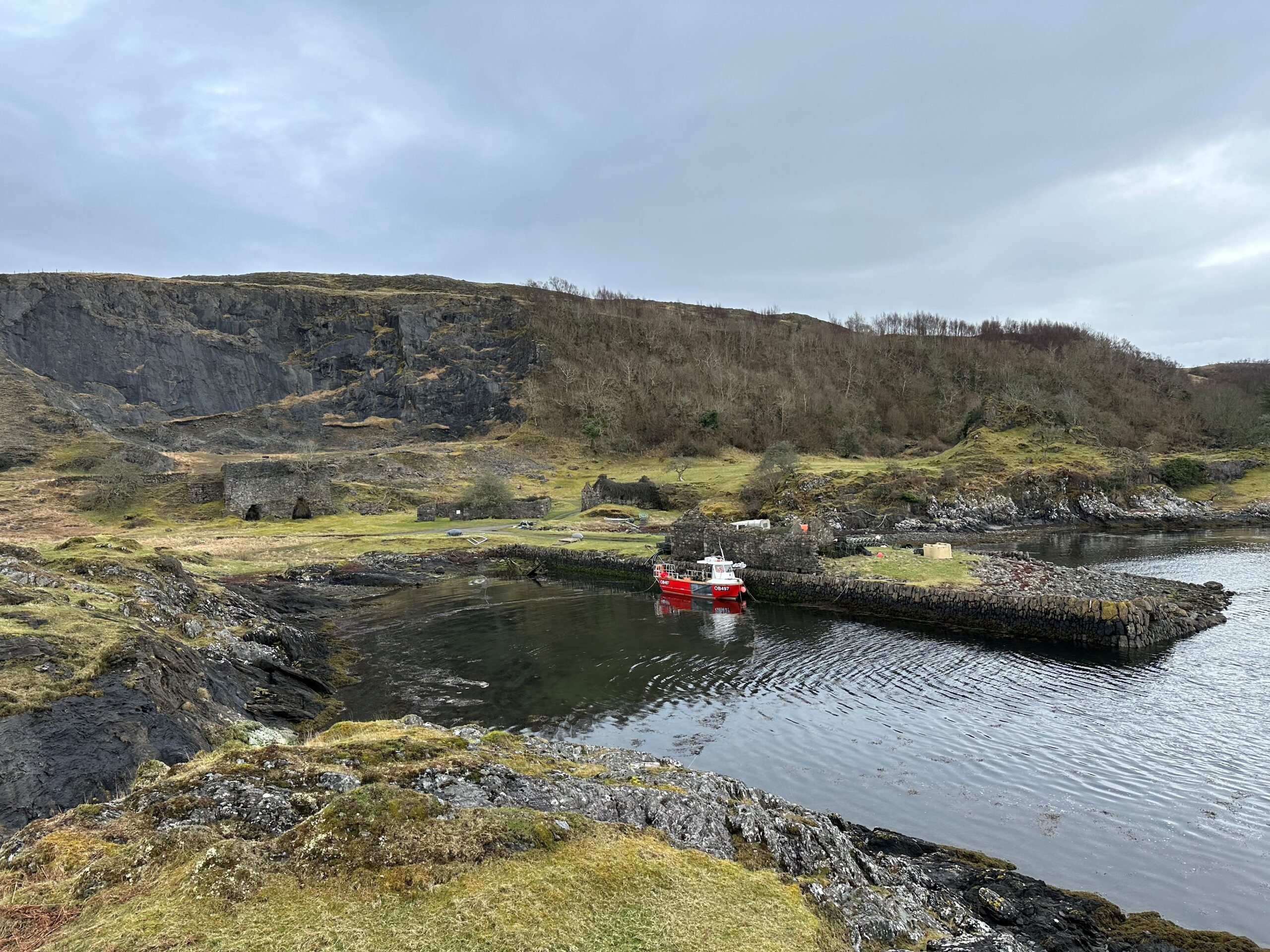 Photo of a small fishing boat moored at a jetty on the edge of an island with visible remnants of industrial lime production