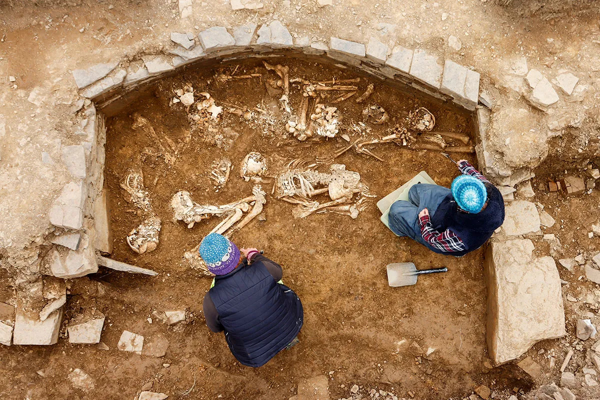 Photo of two people kneeling in a cell (compartment) of a prehistoric grave site under excavation