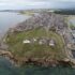 Aerial photograph showing a promontory surrounded by the sea, with a grassy hill area at the end of the promontory and a modern town further back